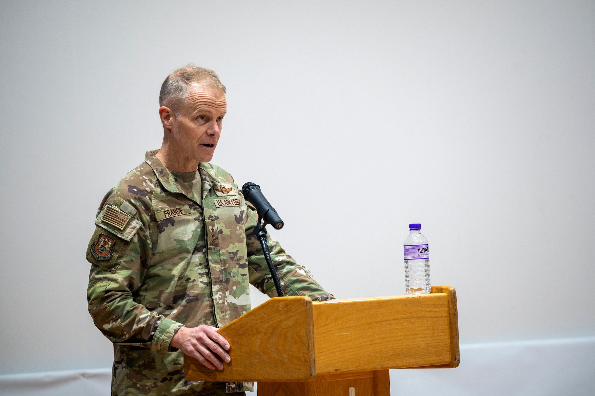 Lt. Gen. France stands left of frame speaking from behind a podium
