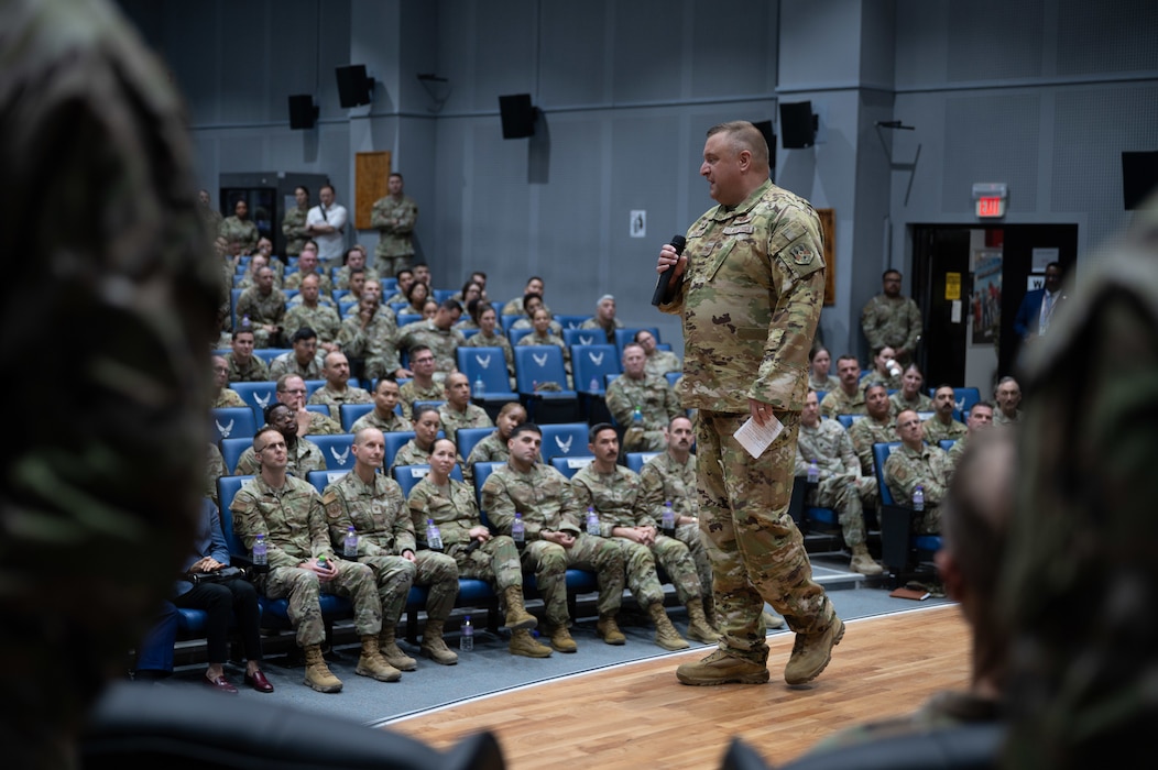 Col. Stouffer mid frame on a stage talking to a crowd of Airmen in front of him