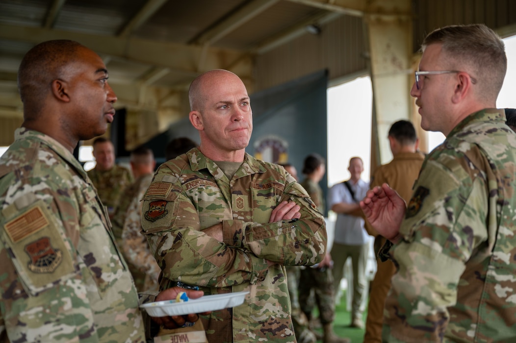 Chief Ski is middle of frame with arms crossed listening attentively to a three-way conversation with Airmen on either side of him