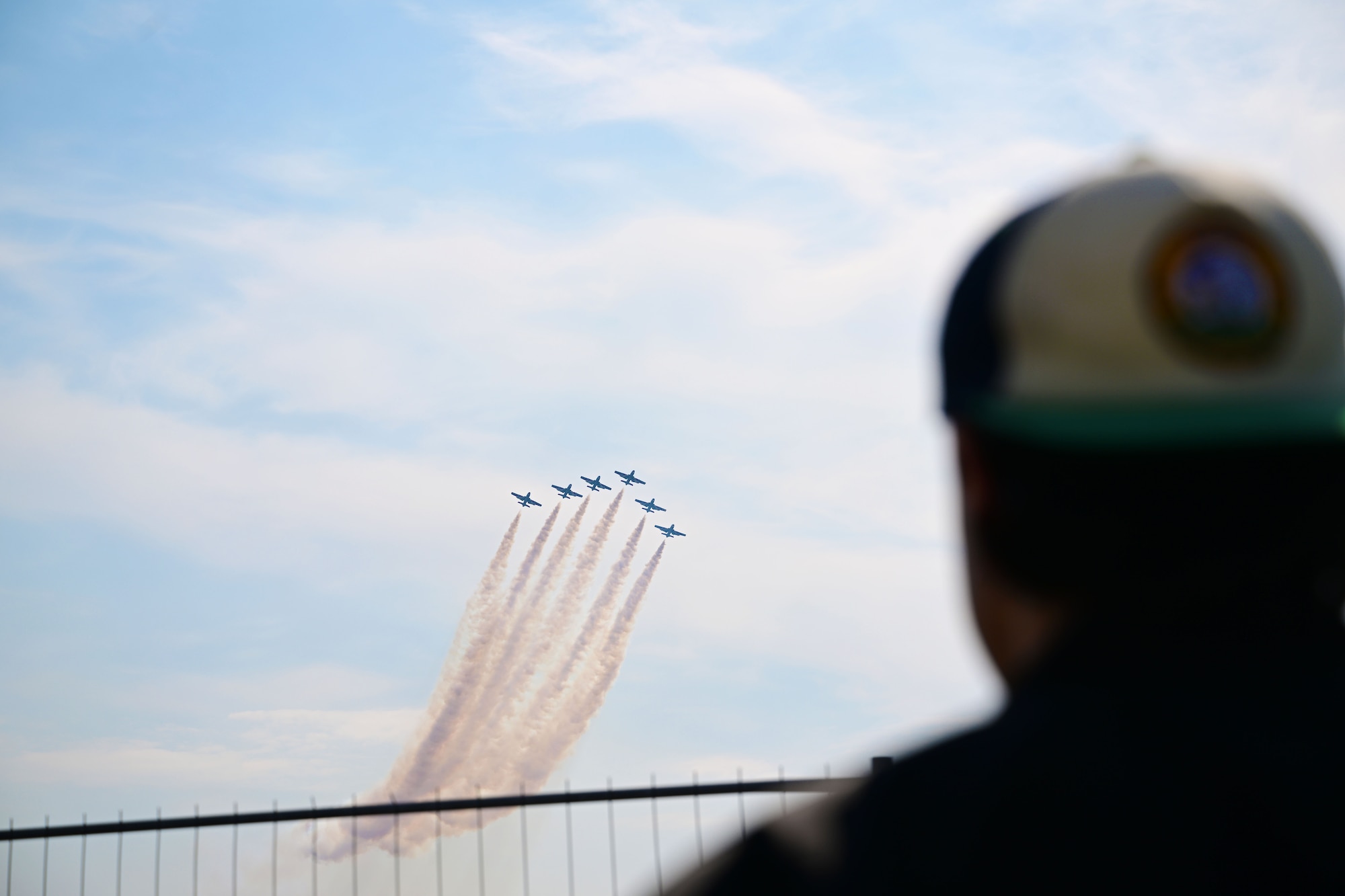 A man watches jets fly across the sky in a formation.
