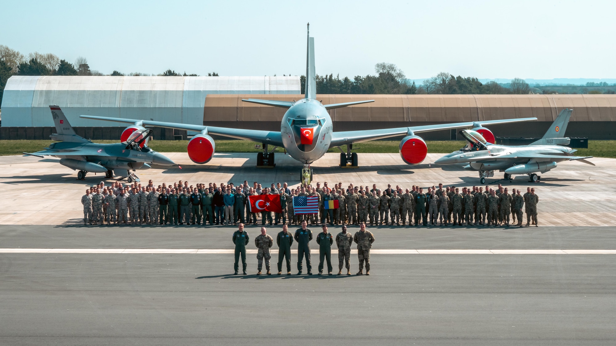 Airmen from the U.S., Türkiye and Romania stand for a group photo in front of two F-16s and a KC-135