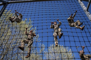 Five soldiers climb up a netted rope under blue skies.