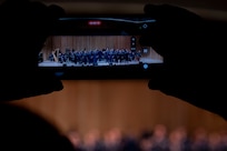 A cellphone records the band in focus as the band is shown burred beyond the phone screen.