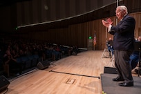 The conductor faces the audience and claps to the beat.