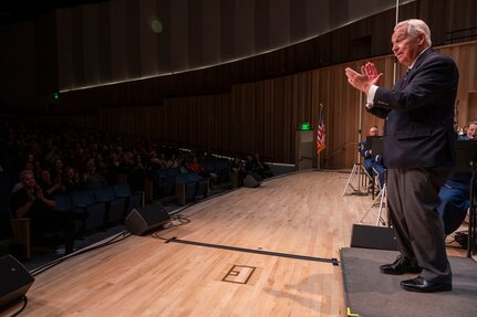 The conductor faces the audience and claps to the beat.