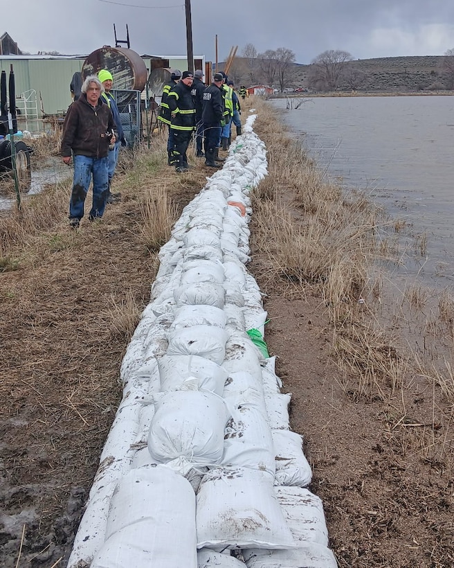 People looking at sandbags that are places on the ground next to water