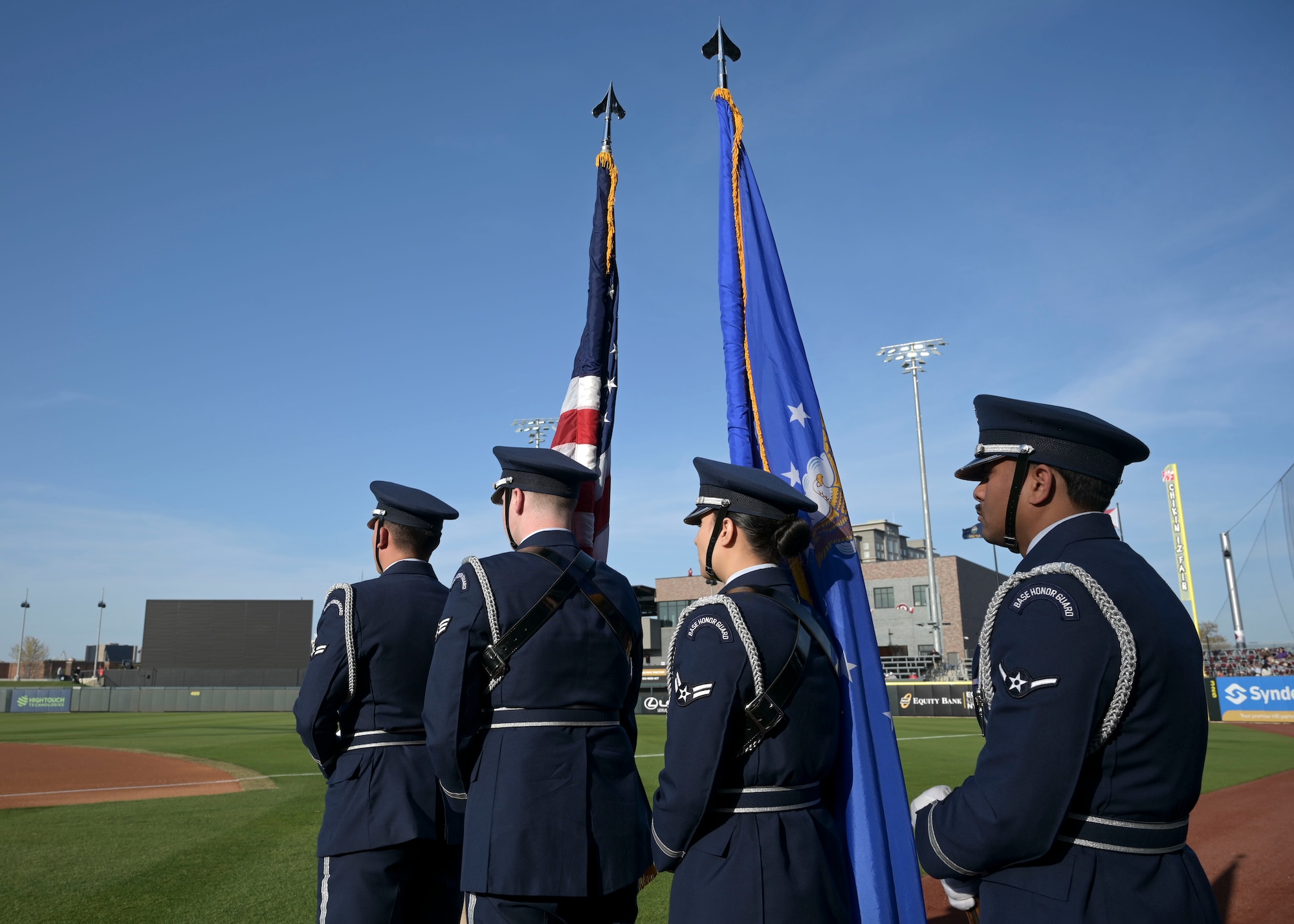 People in military dress uniforms stand in a line with the colors.