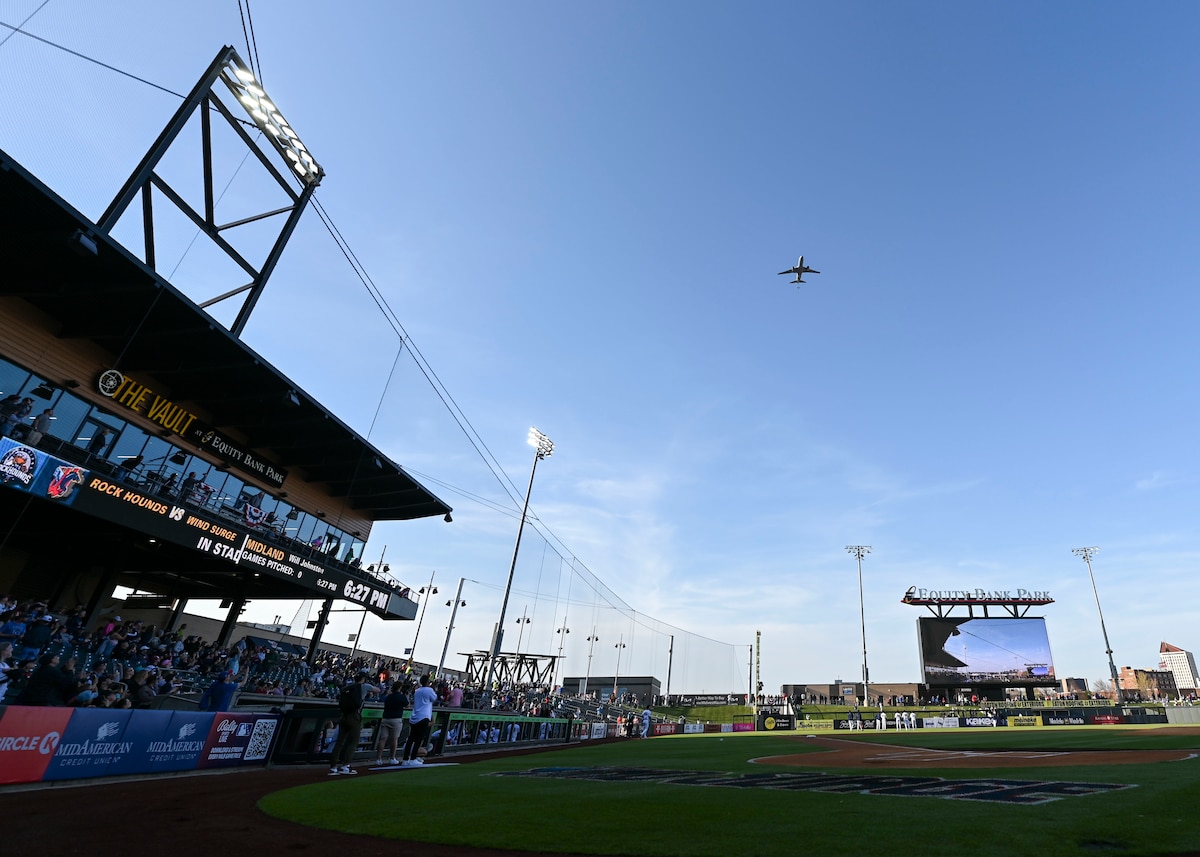 A large military aircraft flies in the sky above a baseball stadium.