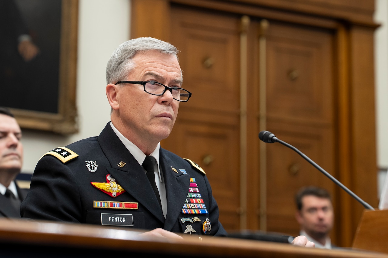 A man in military uniform sits behind a microphone.