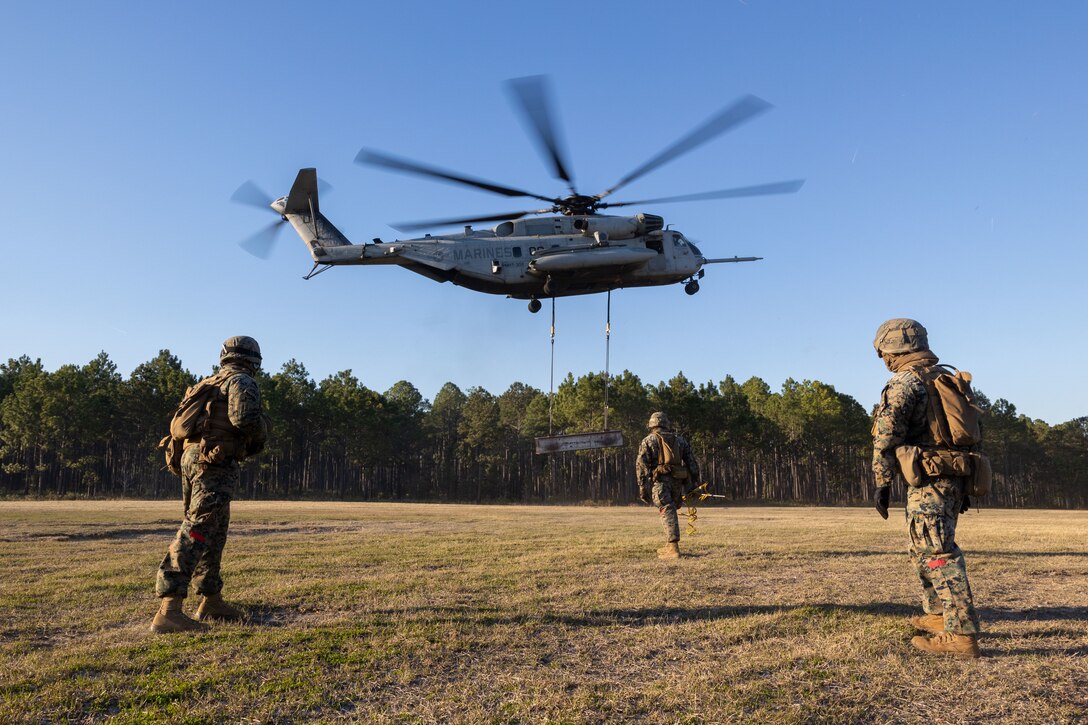 U.S. Marines with Combat Logistics Battalion 25, 4th Marine Logistics Group, look from afar at a CH-53E Super Stallion assigned to Marine Heavy Helicopter Training Squadron 302 (HMHT-302), Marine Aircraft Group 29 (MAG-29), 2nd Marine Aircraft Wing (2nd MAW), carrying an H Beam at Camp Lejeune, North Carolina, Mar. 27, 2025. Landing support specialists and pilots conducted HST to familiarize themselves with insertions and extractions of heavy loads to increase their proficiency in combat scenarios. (U.S. Marine Corps photo by Cpl. Salvador Flores Perez)