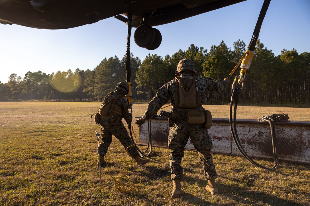 U.S. Marine Corps Cpl. Noah J. McGhee, right, landing support team leader, and Lance Cpl. Refugio Estrella, landing support specialist, both with Combat Logistics Battalion 25, 4th Marine Logistics Group, hook cables from an H Beam onto a CH-53E Super Stallion assigned to Marine Heavy Helicopter Training Squadron 302 (HMHT-302), Marine Aircraft Group 29 (MAG-29), 2nd Marine Aircraft Wing (2nd MAW), during Helicopter Support Team training at Camp Lejeune, North Carolina, Mar. 27, 2025. Landing support specialists and pilots conducted HST to familiarize themselves with insertions and extractions of heavy loads to increase their proficiency in combat scenarios. (U.S. Marine Corps photo by Cpl. Salvador Flores Perez)