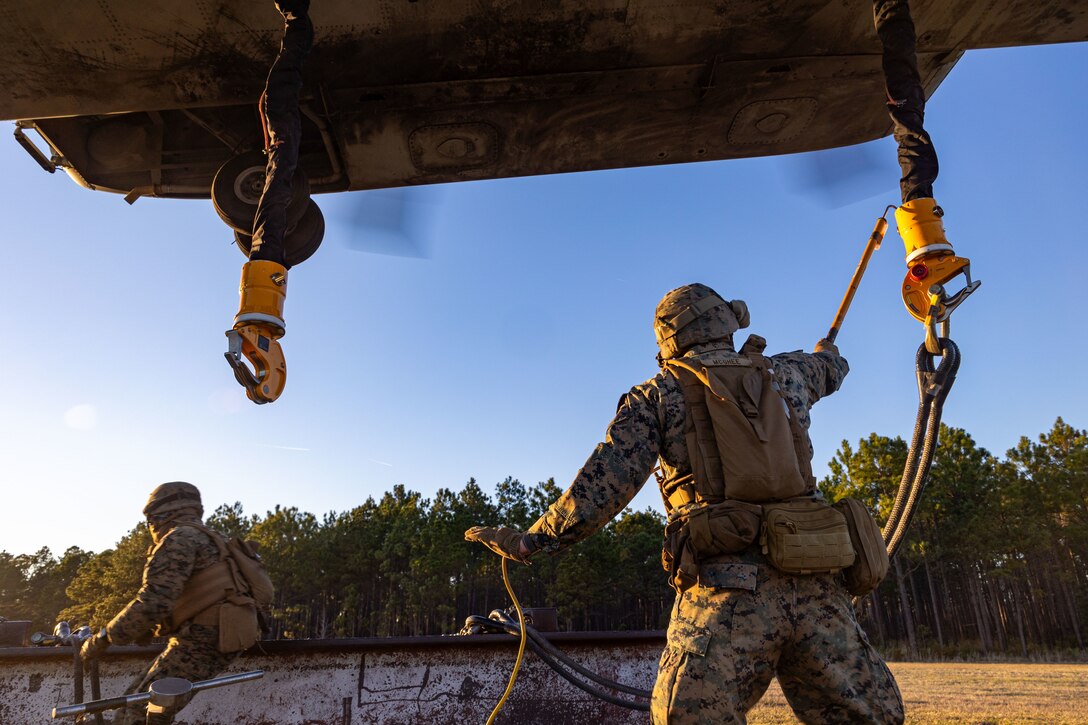 U.S. Marine Corps Cpl. Noah J. McGhee, right, landing support team leader, and Lance Cpl. Refugio Estrella, landing support specialist, both with Combat Logistics Battalion 25, 4th Marine Logistics Group, hook cables onto a CH-53K King Stallion assigned to Marine Heavy Helicopter Squadron 461 (HMH-461), Marine Aircraft Group 29 (MAG-29), 2nd Marine Aircraft Wing (2nd MAW), during a helicopter support team training at Camp Lejeune, North Carolina, Mar. 27, 2025. Landing support specialists and pilots conducted HST to familiarize themselves with insertions and extractions of heavy loads to increase their proficiency in combat scenarios. (U.S. Marine Corps photo by Cpl. Salvador Flores Perez)