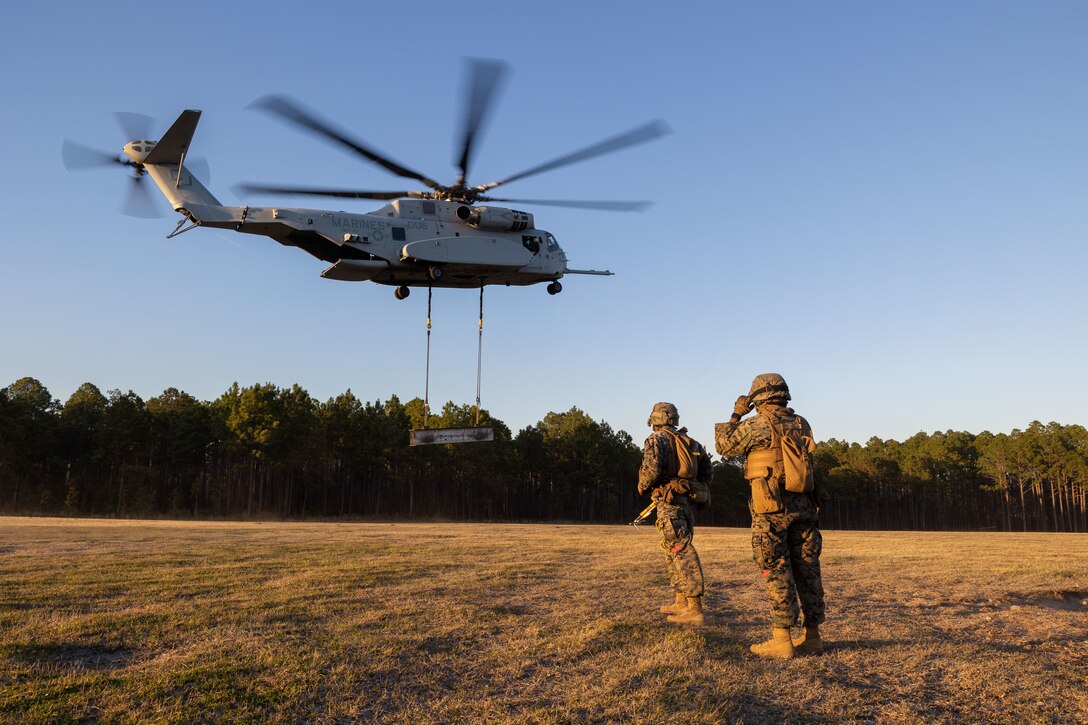 U.S. Marine Corps Cpl. Noah J. McGhee, left, landing support team leader, and Lance Cpl. Refugio Estrella, landing support specialist, both with Combat Logistics Battalion 25, 4th Marine Logistics Group, look from afar at a CH-53K King Stallion assigned to Marine Heavy Helicopter Squadron 461 (HMH-461), Marine Aircraft Group 29 (MAG-29), 2nd Marine Aircraft Wing (2nd MAW), carrying an H Beam at Camp Lejeune, North Carolina, Mar. 27, 2025. Landing support specialists and pilots conducted HST to familiarize themselves with insertions and extractions of heavy loads to increase their proficiency in combat scenarios. (U.S. Marine Corps photo by Cpl. Salvador Flores Perez)