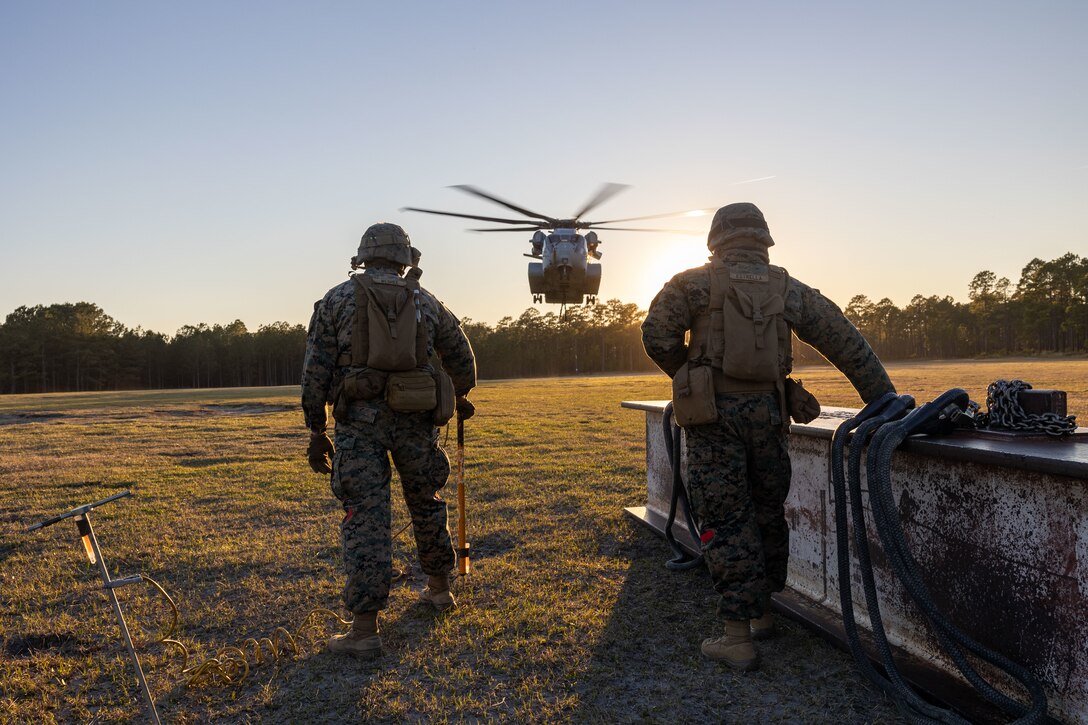 U.S. Marine Corps Cpl. Noah J. McGhee, left, landing support team leader, and Lance Cpl. Refugio Estrella, landing support specialist, both with Combat Logistics Battalion 25, 4th Marine Logistics Group, look towards an approaching CH-53K King Stallion assigned to Marine Heavy Helicopter Squadron 461 (HMH-461), Marine Aircraft Group 29 (MAG-29), 2nd Marine Aircraft Wing (2nd MAW), during a helicopter support team training at Camp Lejeune, North Carolina, Mar. 27, 2025. Landing support specialists and pilots conducted HST to familiarize themselves with insertions and extractions of heavy loads to increase their proficiency in combat scenarios. (U.S. Marine Corps photo by Cpl. Salvador Flores Perez)