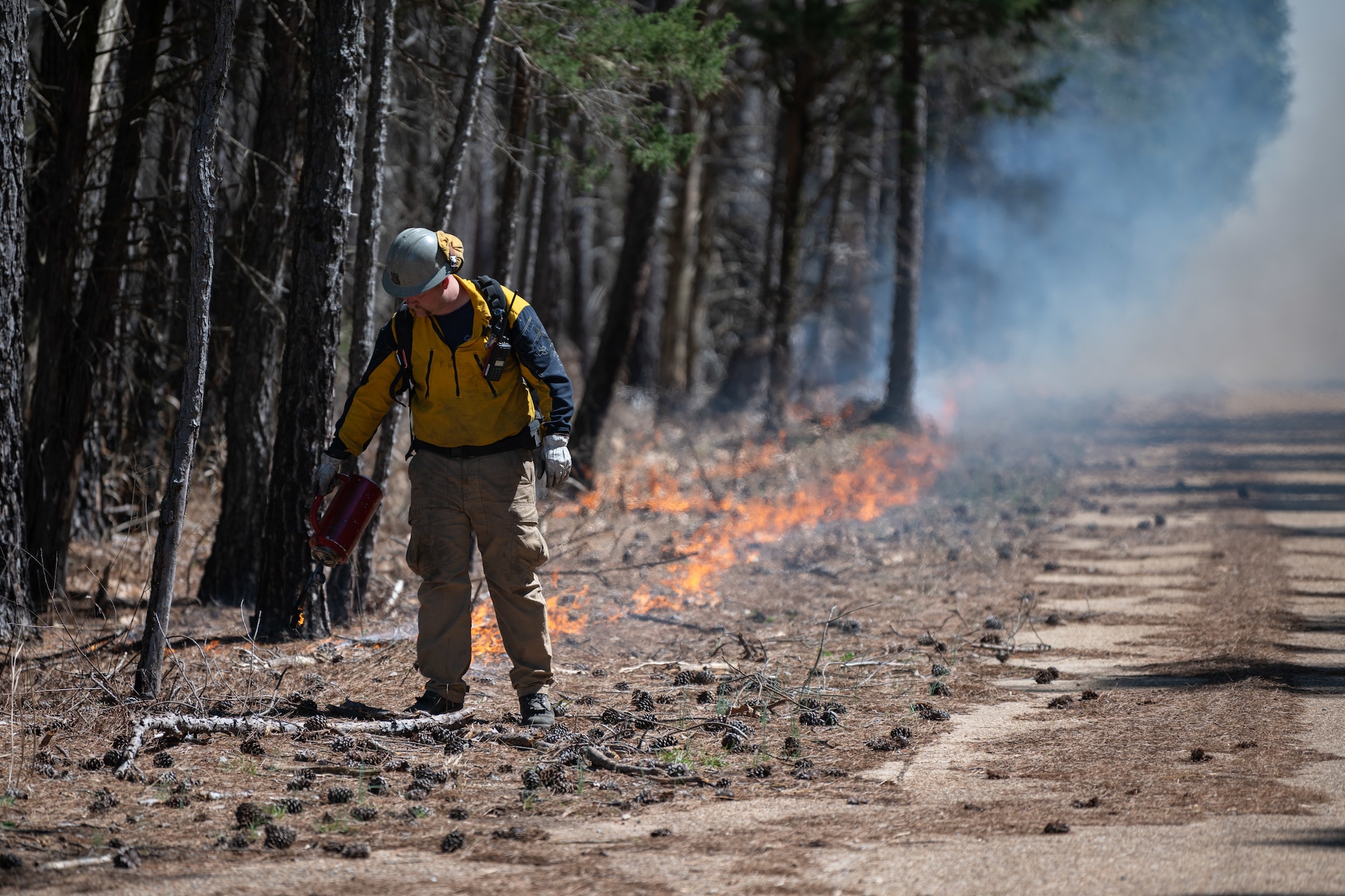 Tyler Turner with the Beale AFB, USAF Wildland Fire Branch, ignites foliage to execute a prescribed burn on acreage surrounding Arnold AFB, Tenn., March 26, 2025. The prescribed burn prevents overgrowth of foliage on the forest floor and offers valuable training to the participating personnel. (U.S. Air Force photo by Keith Thornburgh)