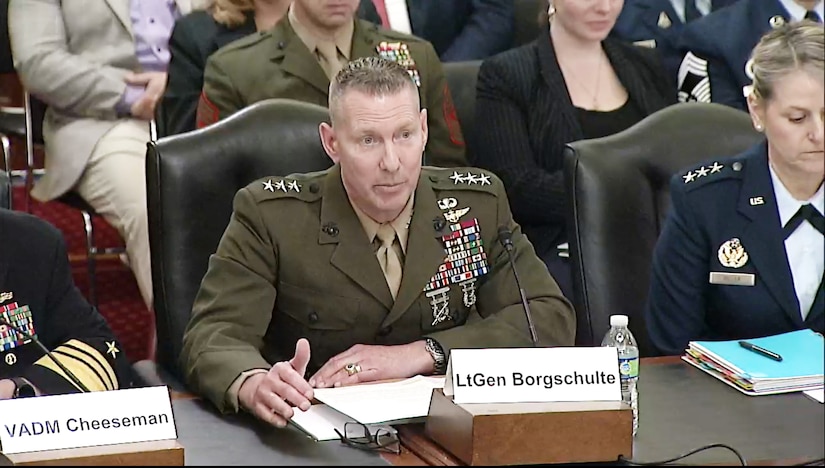 A man in a military uniform sits at a wooden table.