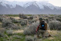ROTC student with weapon stands guard kneeling with mountain background
