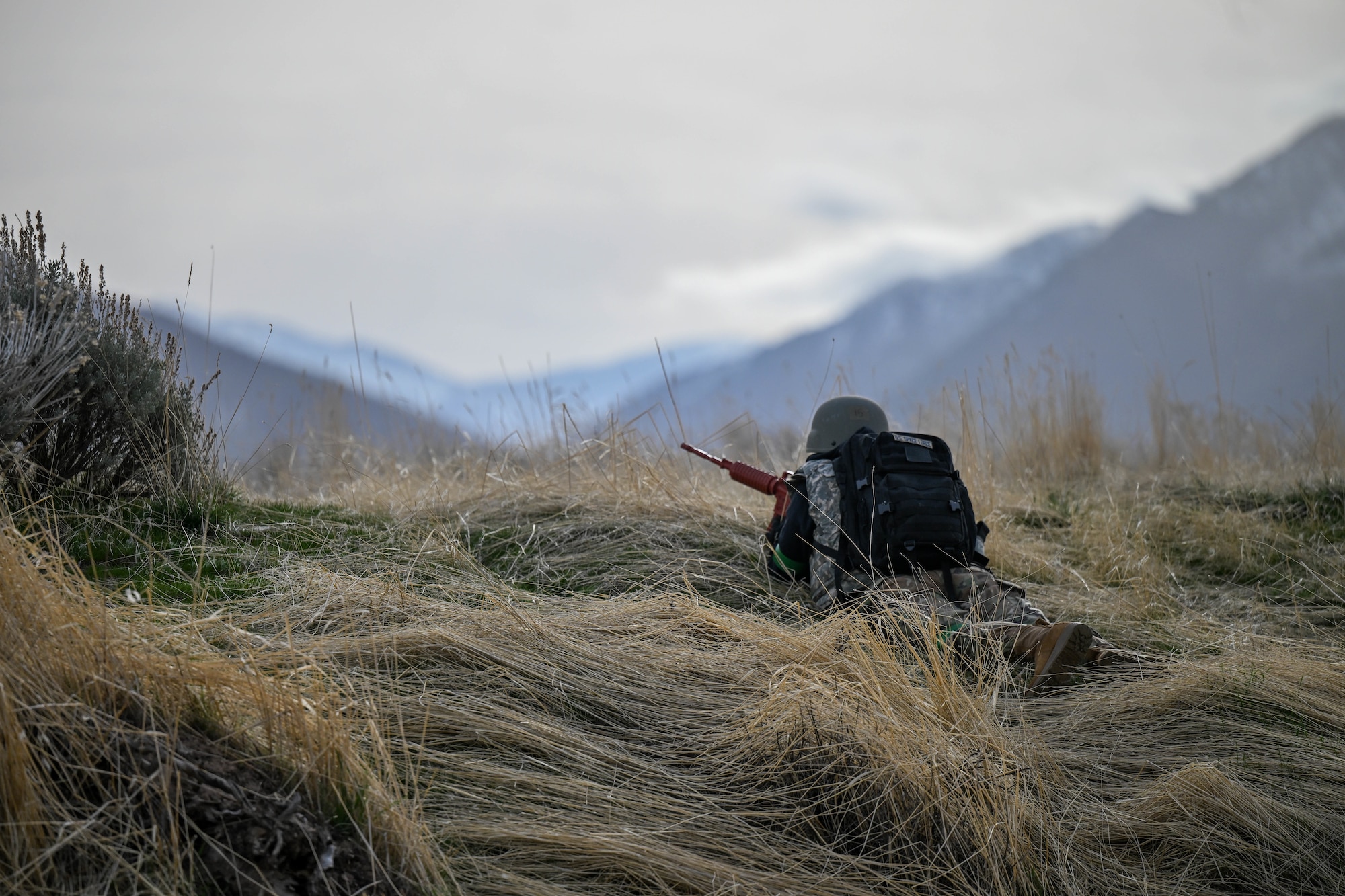 ROTC student lays on ground with weapon standing guard with a mountain background