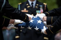 Army Soldiers wearing dark ceremonial uniforms with white gloves are folding a US flag.