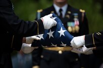 Army soldiers wearing dark ceremonial uniforms with white gloves are folding a US flag.