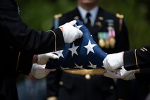 Army soldiers wearing dark ceremonial uniforms with white gloves are folding a US flag.