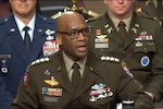 A man in a military uniform and eyeglasses sits behind a microphone delivering testimony.