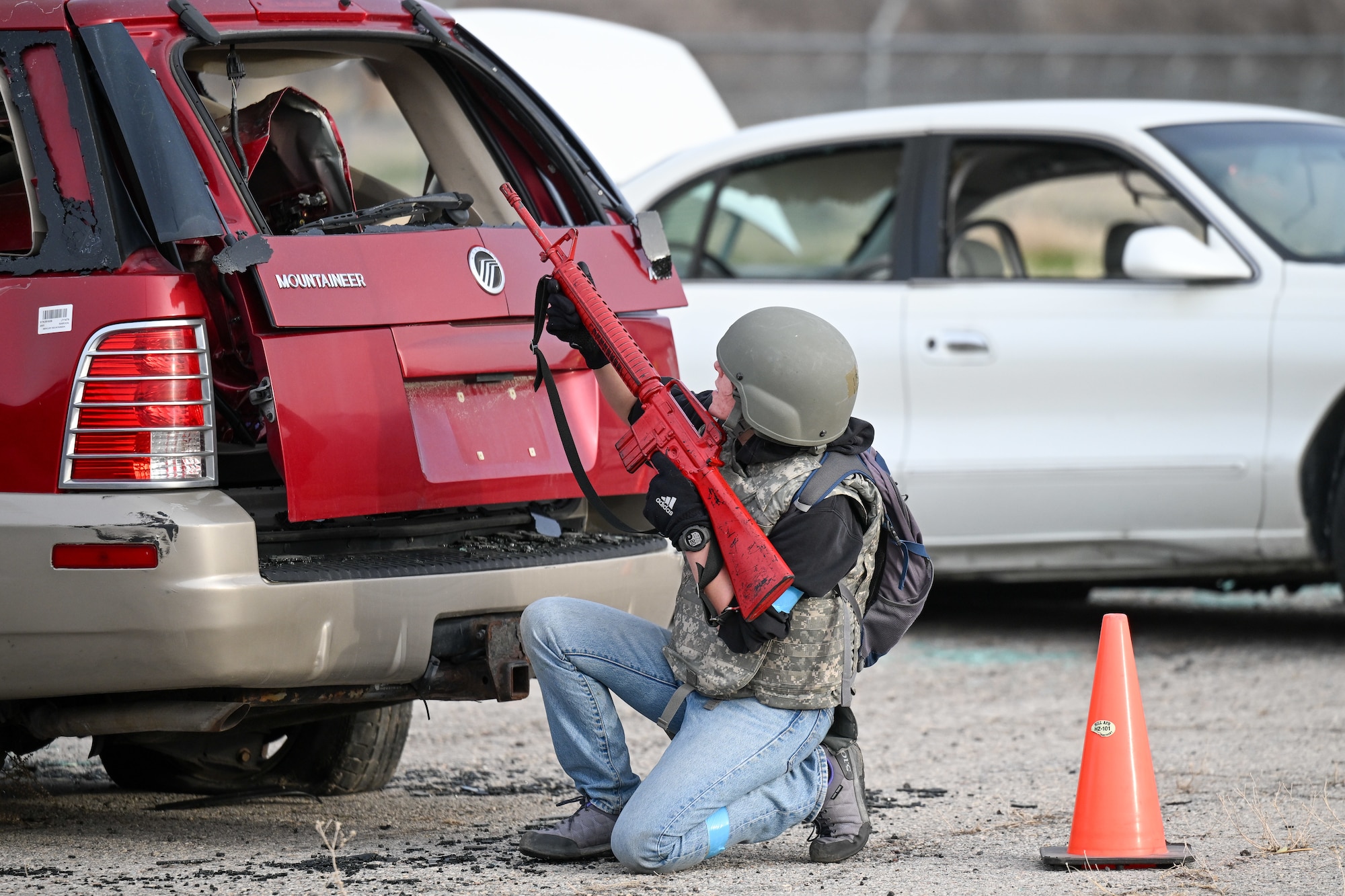 ROTC cadet with a weapon kneeling behind a vehicle for cover