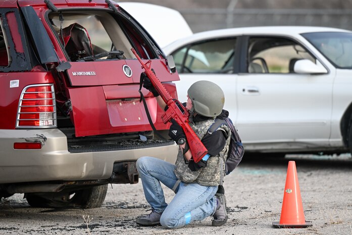 ROTC cadet with a weapon kneeling behind a vehicle for cover