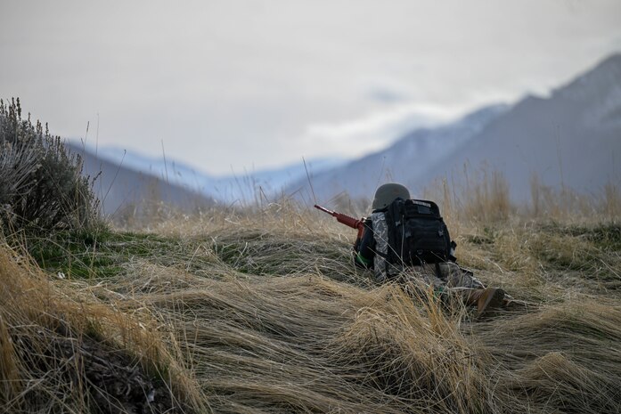 ROTC student lays on ground with weapon standing guard with a mountain background