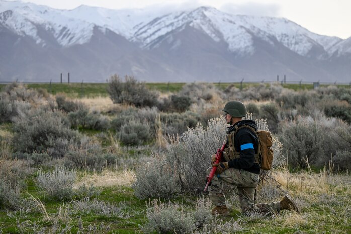 ROTC student with weapon stands guard kneeling with mountain background