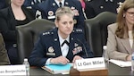 A woman in a military uniform sits at a wooden table.