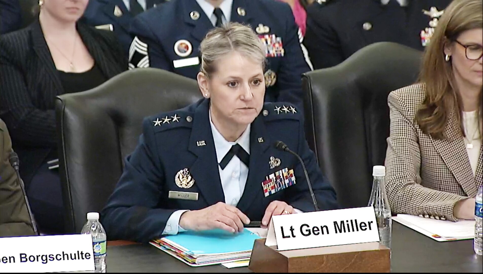 A woman in a military uniform sits at a wooden table.