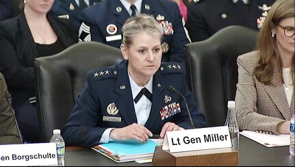 A woman in a military uniform sits at a wooden table.