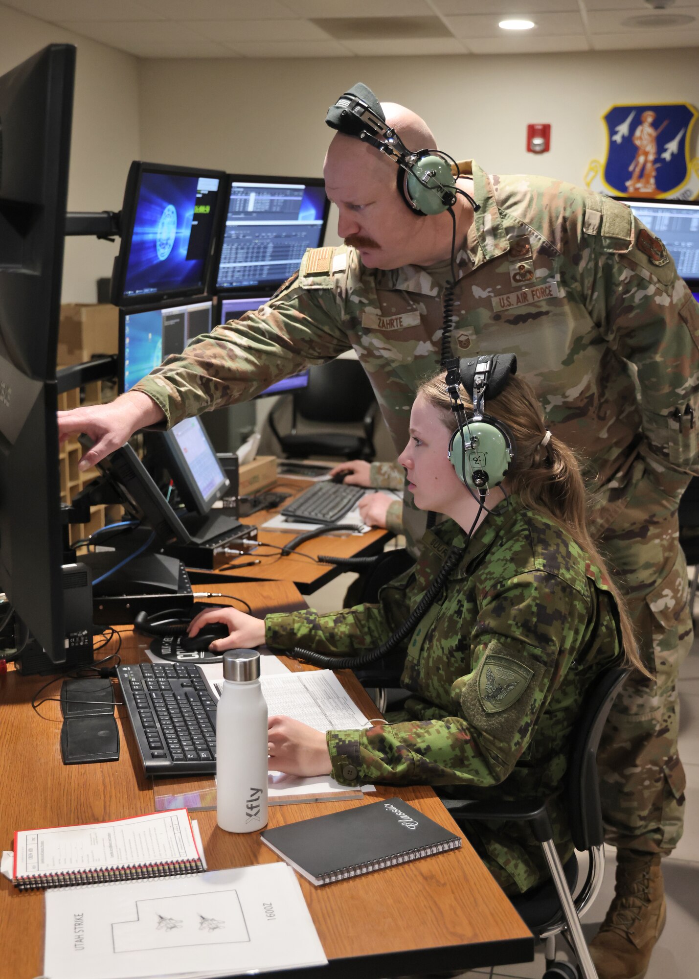 U.S. Air Force Master Sgt. Kody Zahrte, a weapons director assigned to the Wisconsin Air National Guard's 128th Air Control Squadron, assists 2nd. Lt. Gete Suurraid, a fighter controller with the Estonian Air Force March 31, 2025, during an airspace control training mission conducted with U.S. and NATO crewmembers at Volk Field Air National Guard Base in Camp Douglas, Wisconsin.