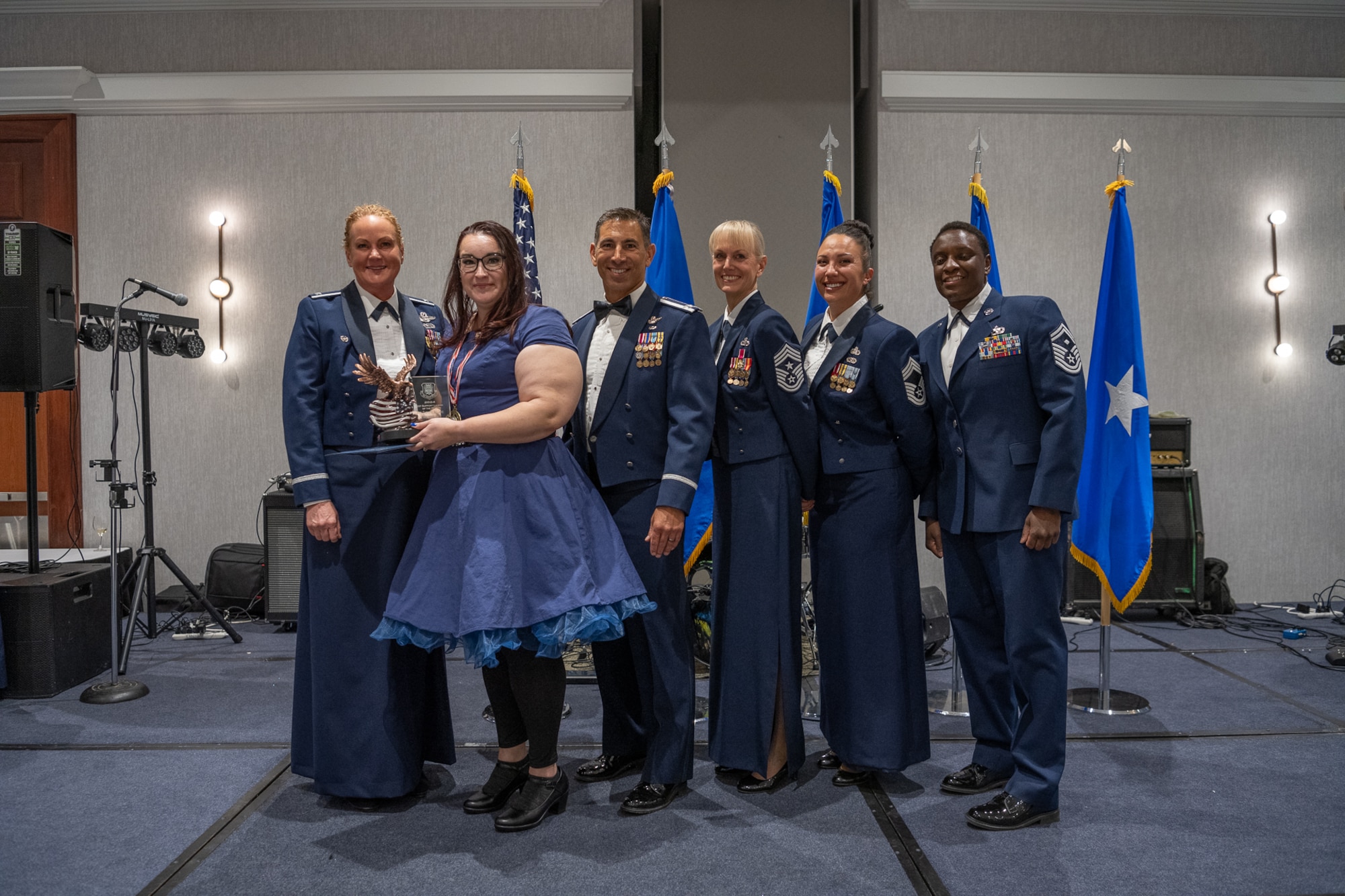A row of servicemembers and one civilian stand together on stage.