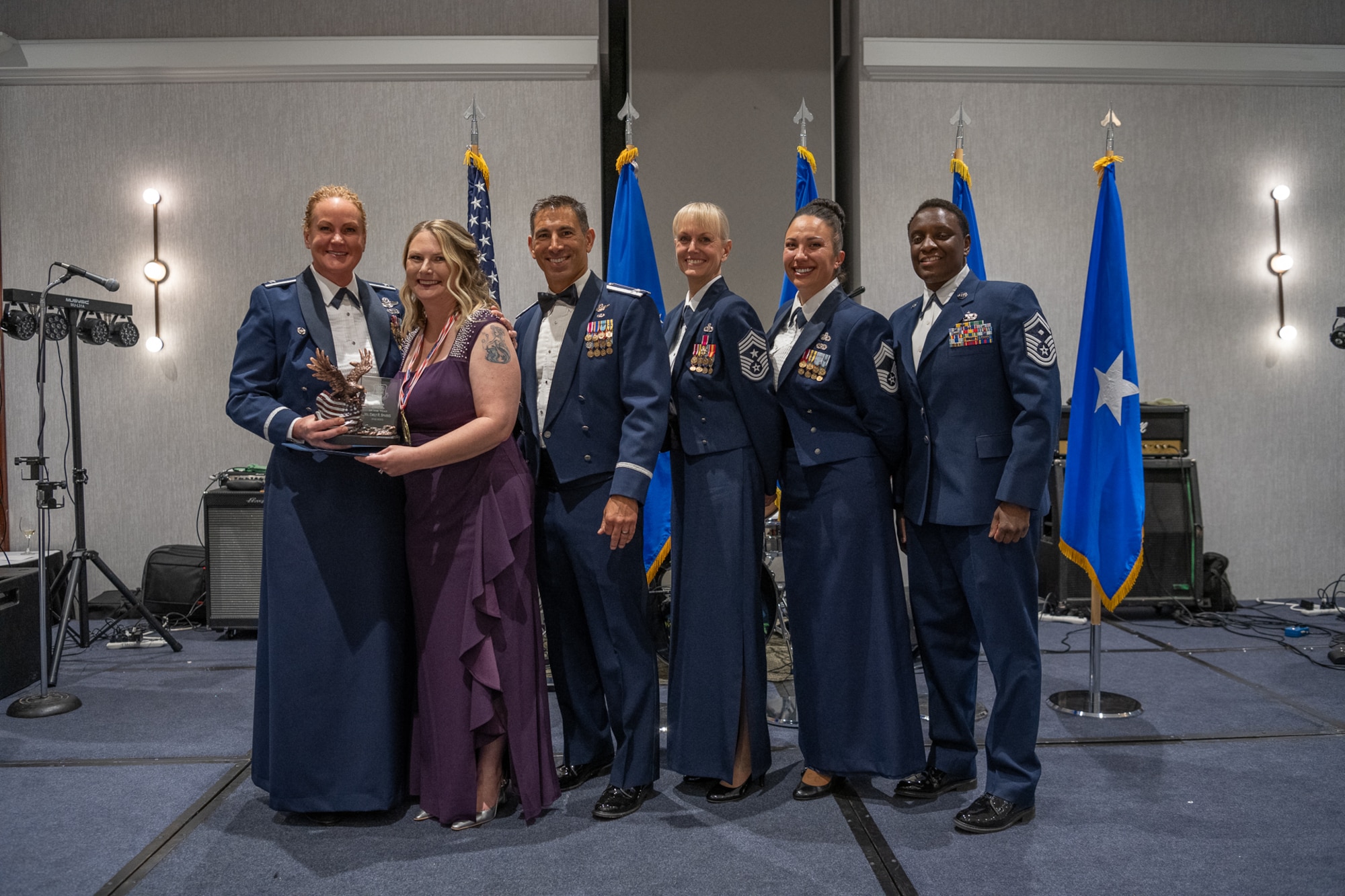A row of servicemembers and one civilian stand together on stage.