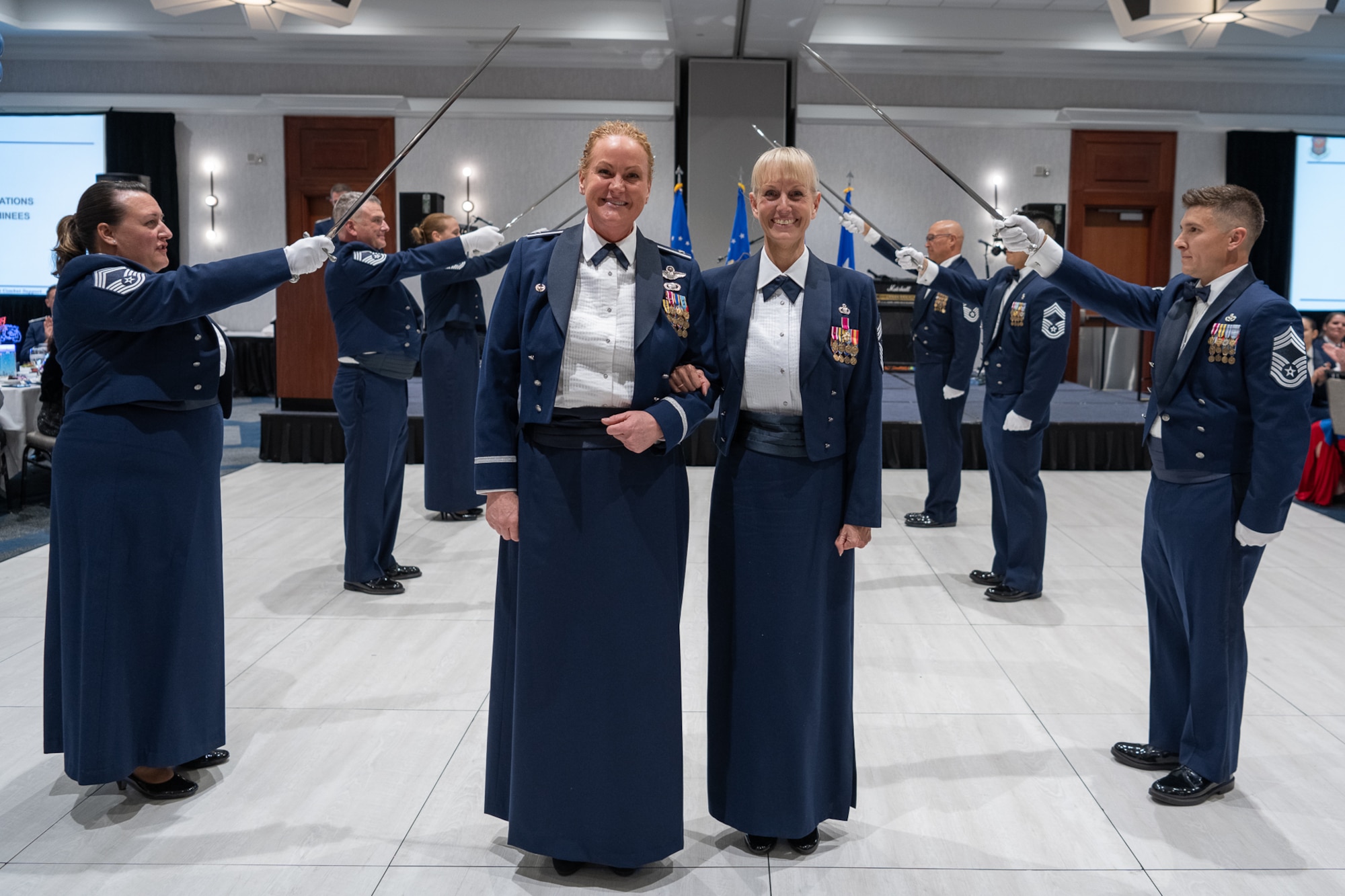 Two servicemembers stand under an archway of swords held by additional servicemembers standing behind them.