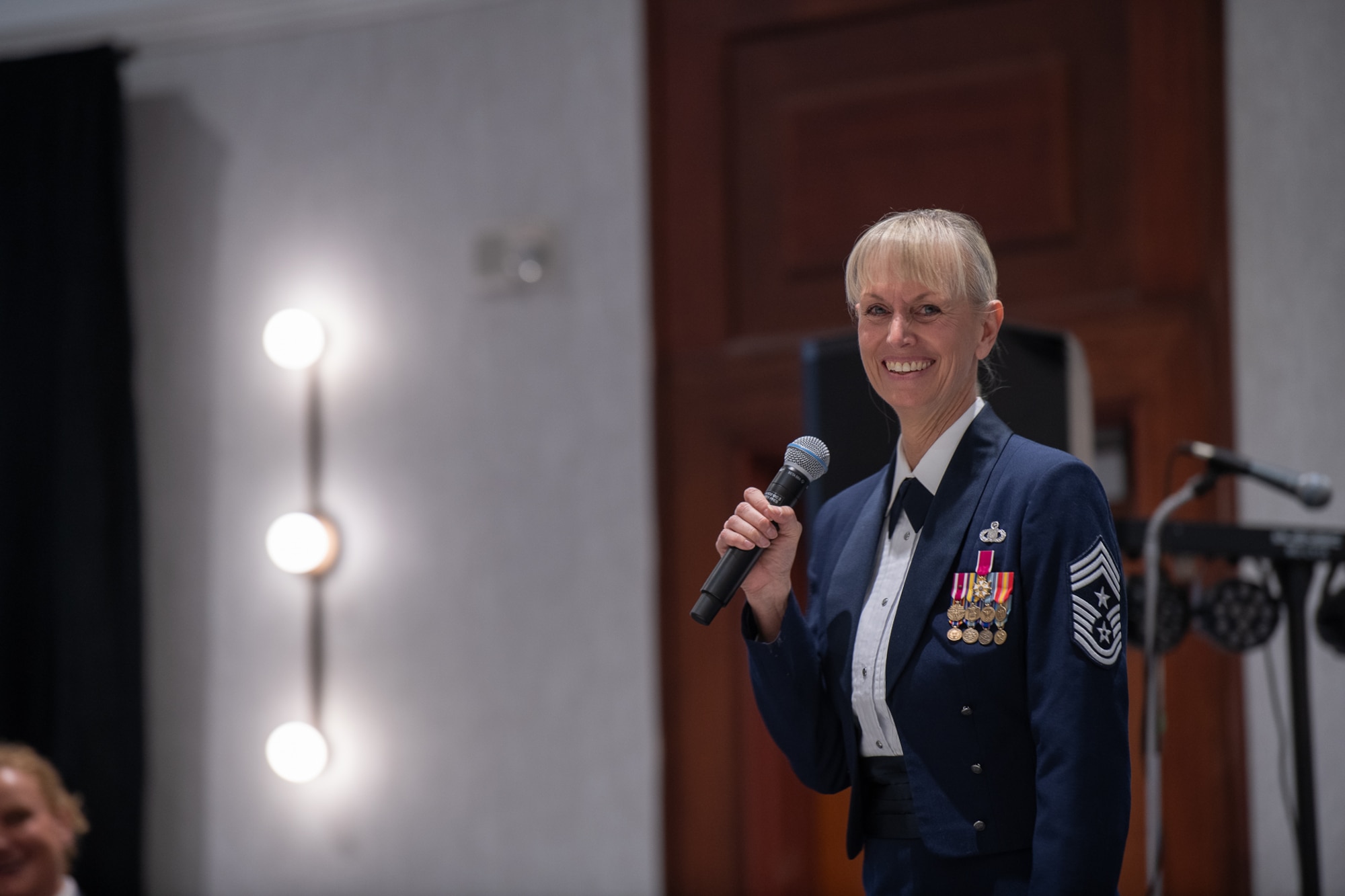 A servicemember holds a microphone while standing in a ballroom.