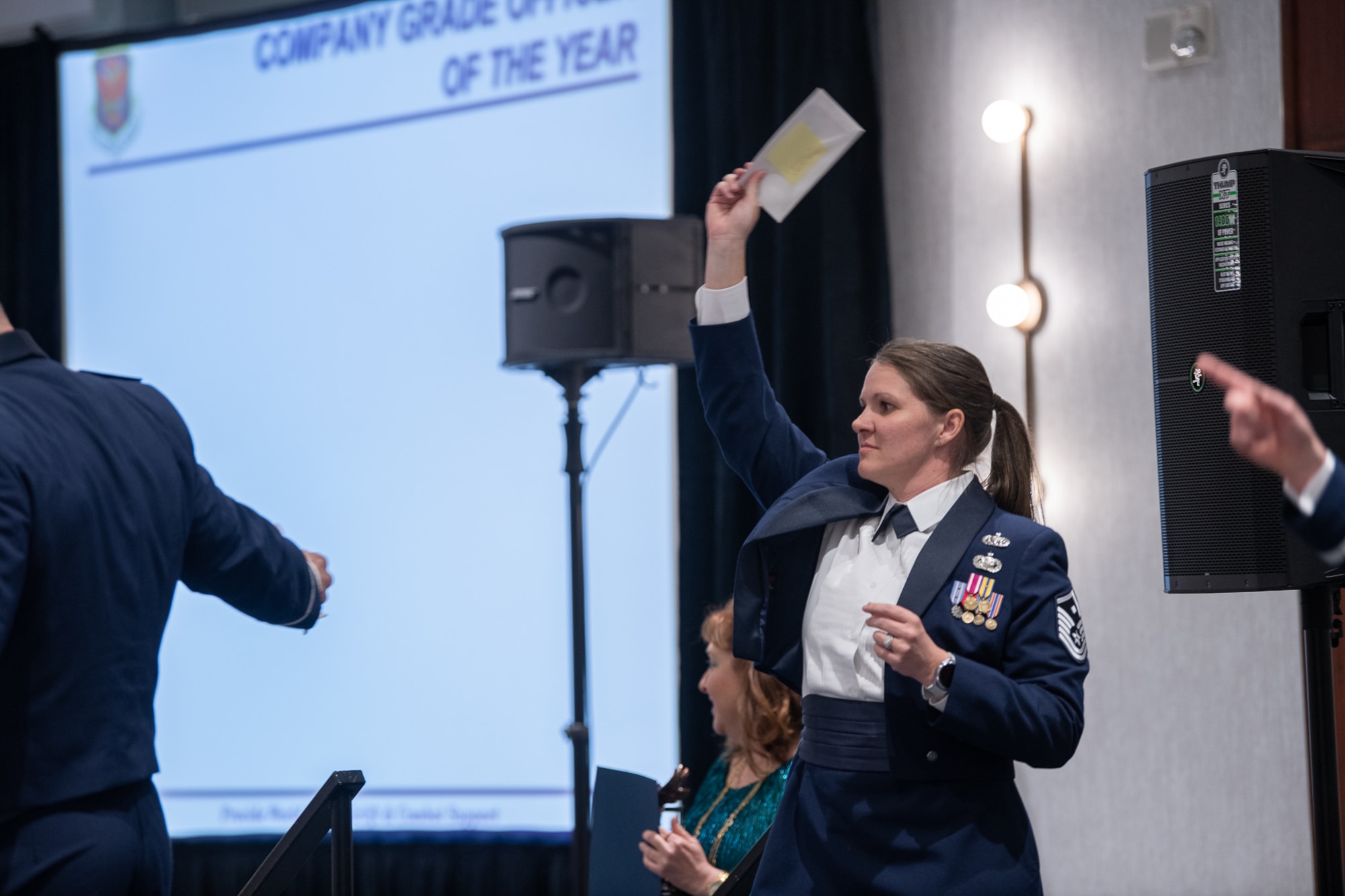 A servicemember holds her hand high containing an envelope.