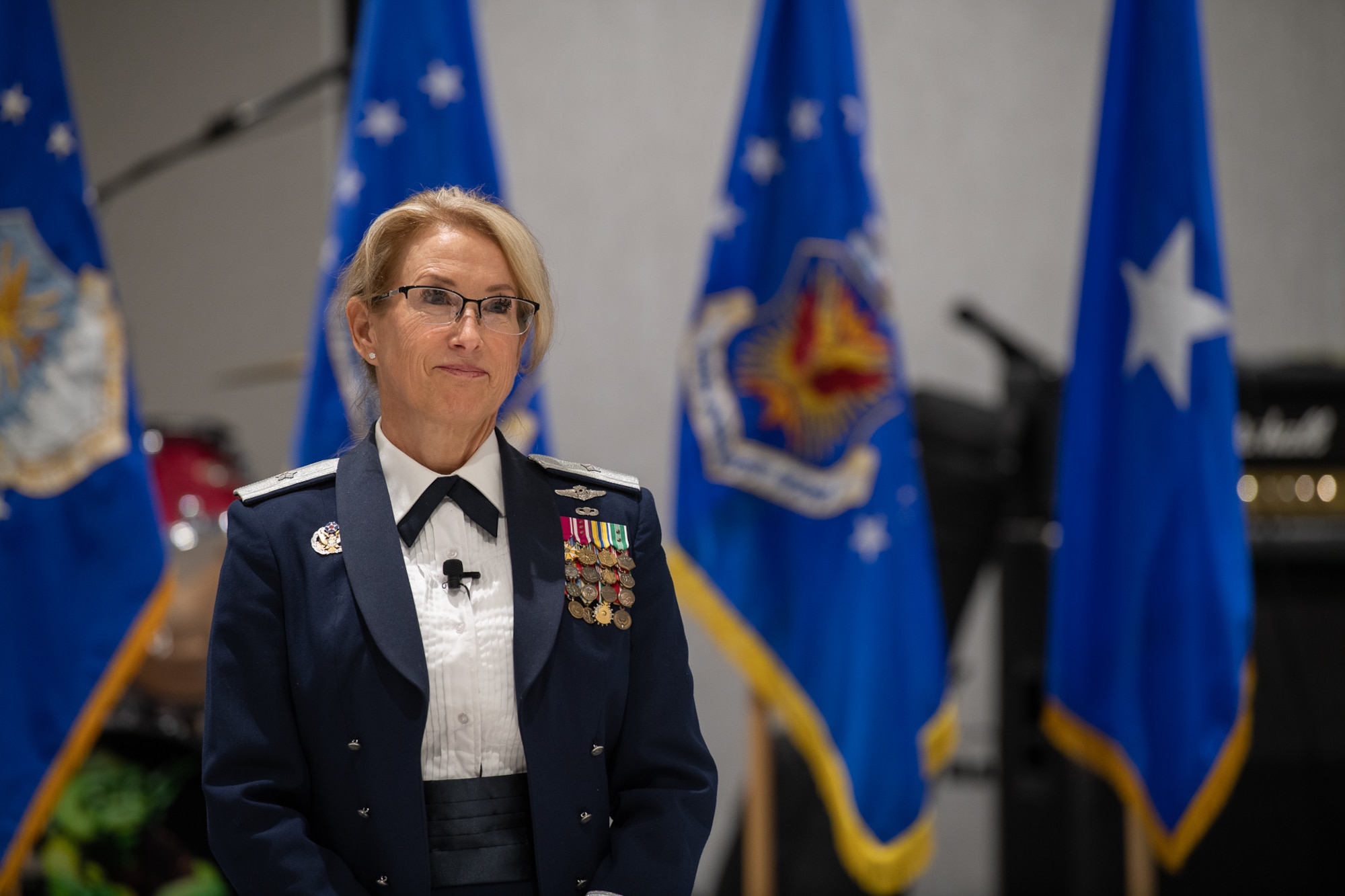 A servicemember stands in front of four flags, one of them a one-star general flag.