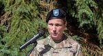 A woman wearing a black beret and a Army OCP uniform speaks at a podium outside.