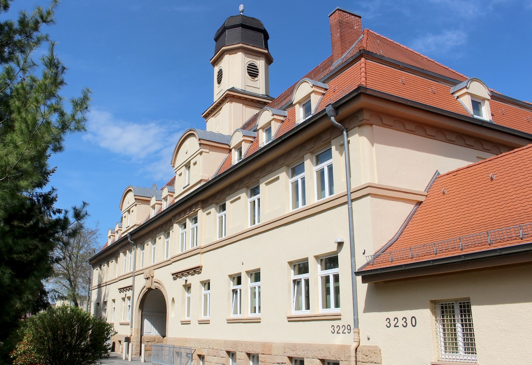 A tan ornate German building with a red roof on a sunny day shown at an angle.