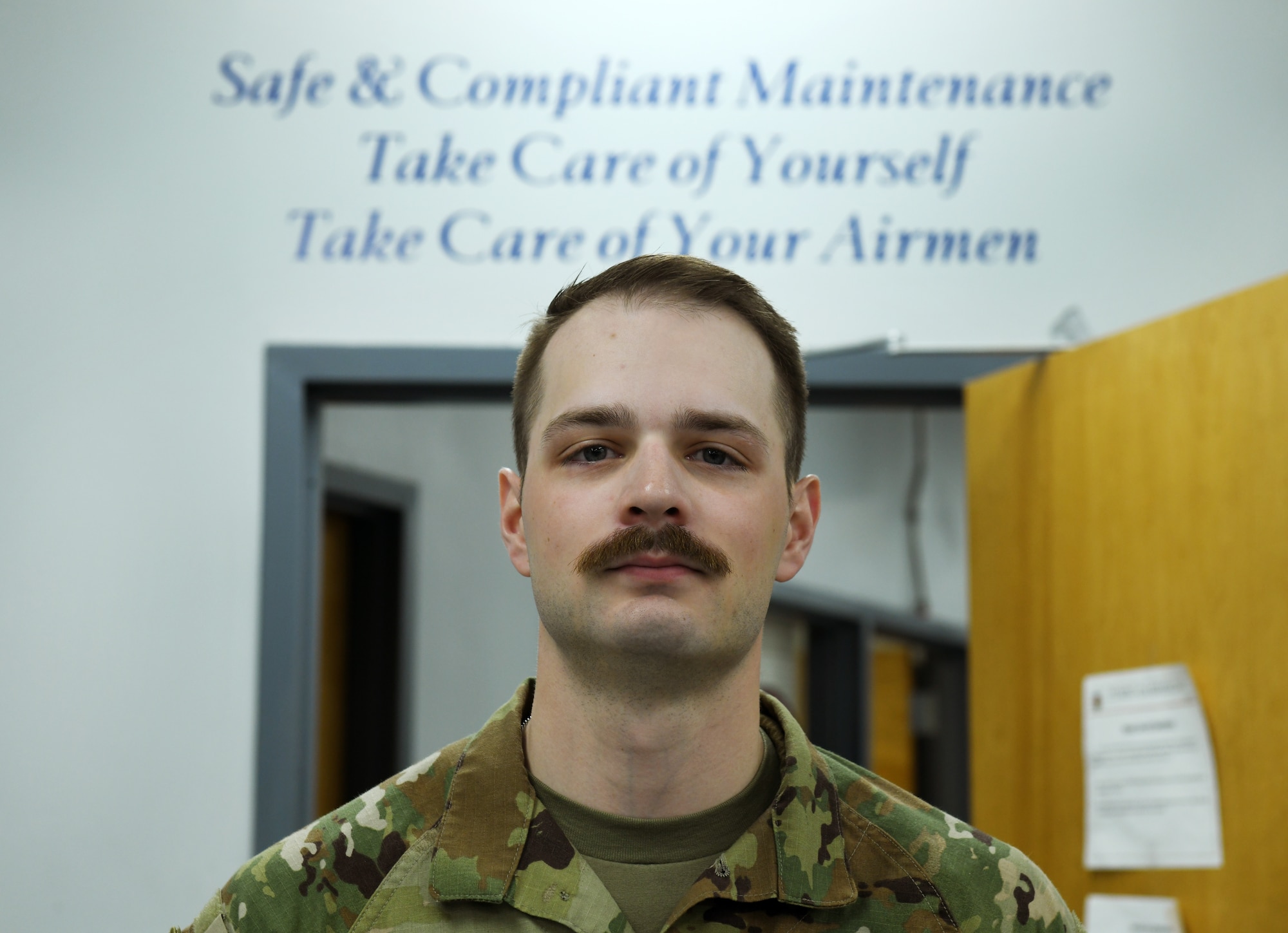 Airman stands in front of 55th Maintenance Group motto for their maintainers.