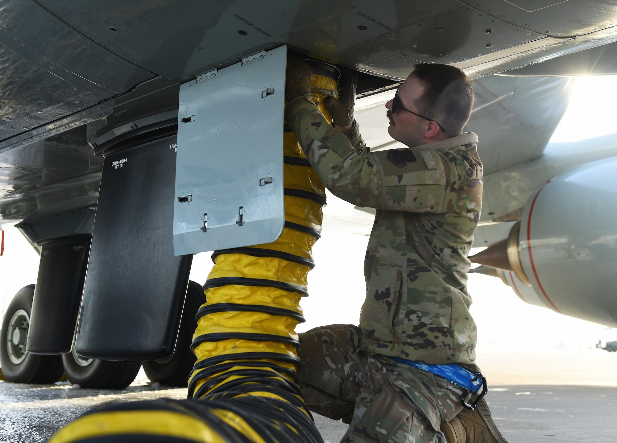 Airman connects external belly air hose during preflight checks inside of a RC-135 Rivet Joint aircraft.
