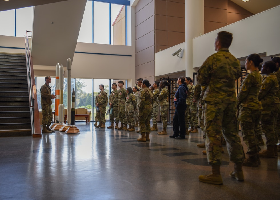 military members in ocps surrounding in an open lobby with rocket models, and a man explaining them