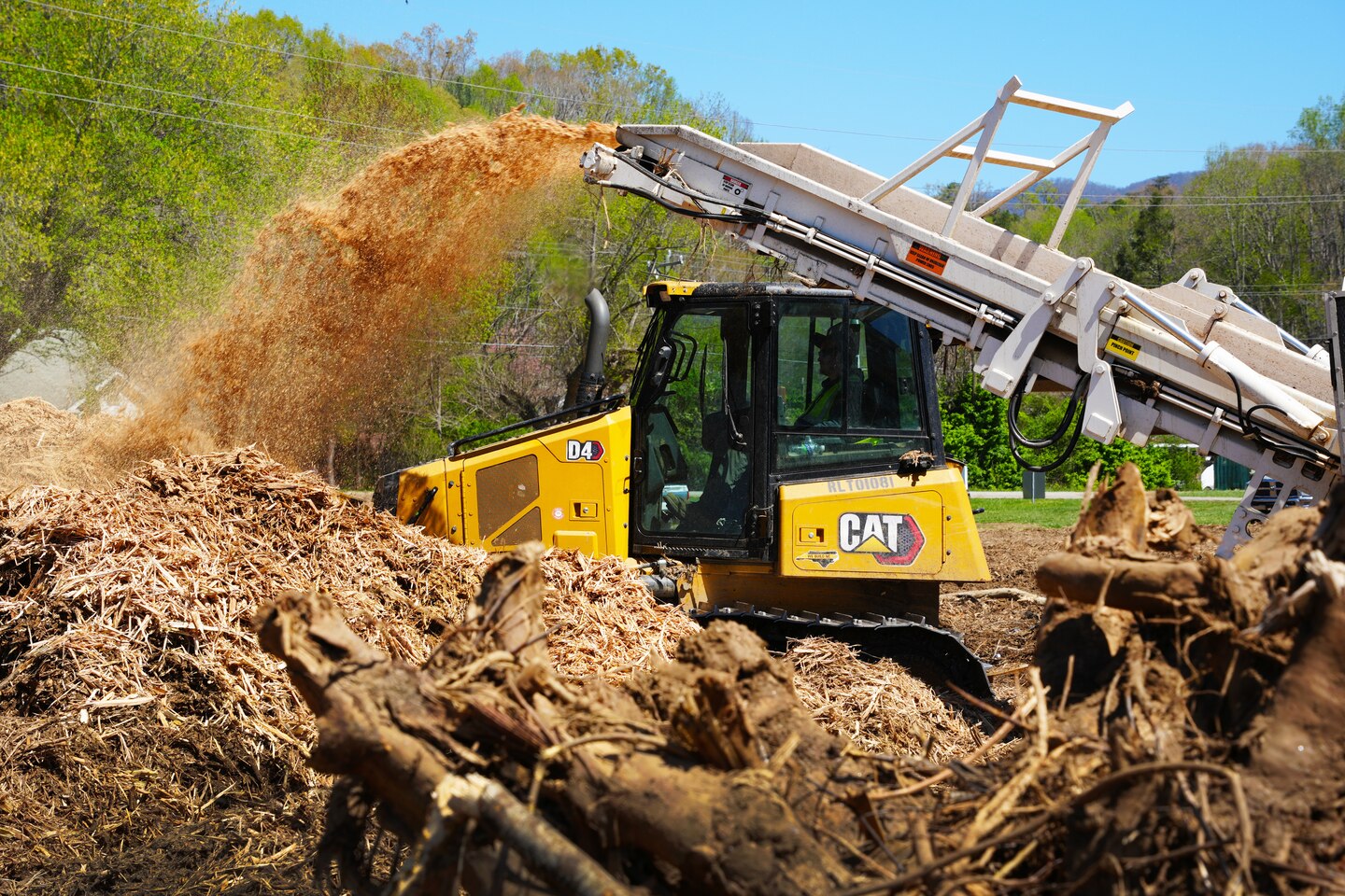 A bulldozer stands ready to move mulch into place as ground debris exits the grinder's conveyor system at the Old Fort Debris Management Site in Old Fort, North Carolina, April 9, 2025. The debris was collected from waterways and rights-of-way impacted by Hurricane Helene.