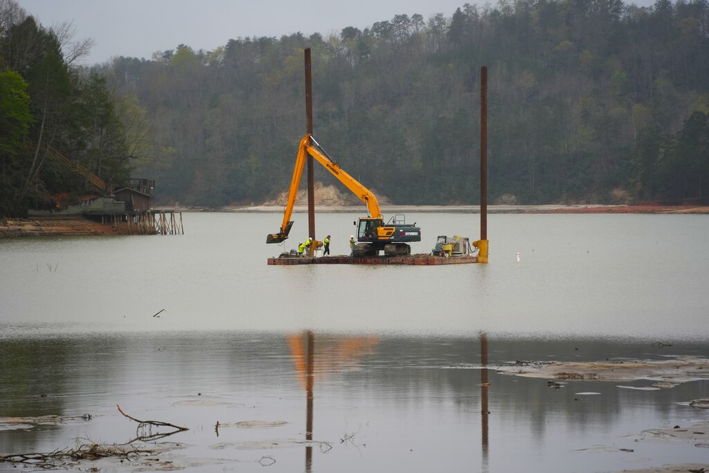Contractors supporting the U.S. Army Corps of Engineers remove sediment from Lake Lure and the Broad River to restore navigability in support of Hurricane Helene recovery operations in Western North Carolina, April 2, 2025. Using heavy equipment such as excavators and rock trucks, crews are creating a passable waterway for barges to access and remove submerged debris. This sediment removal effort is a key step toward restoring safe conditions for the local community and facilitating long-term recovery.