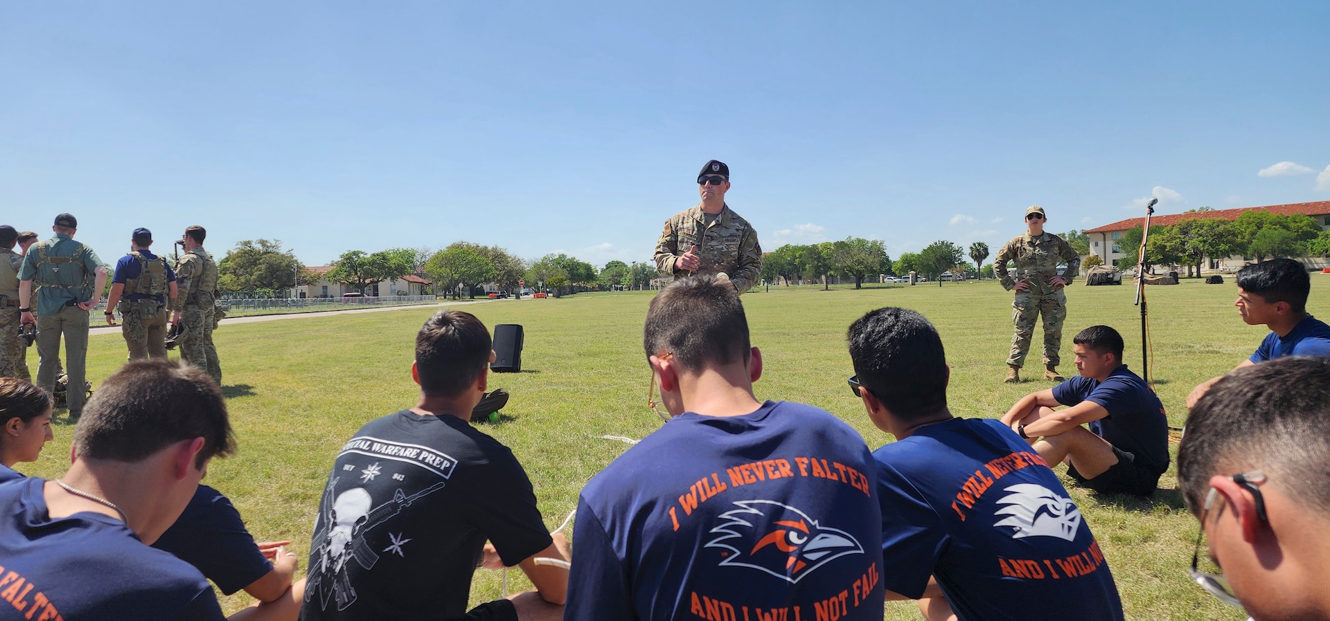 servicemember stands while students are seated on ground