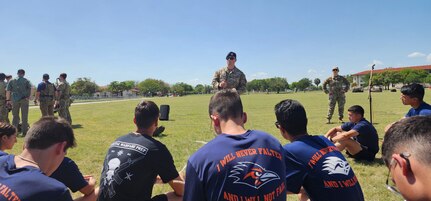 servicemember stands while students are seated on ground