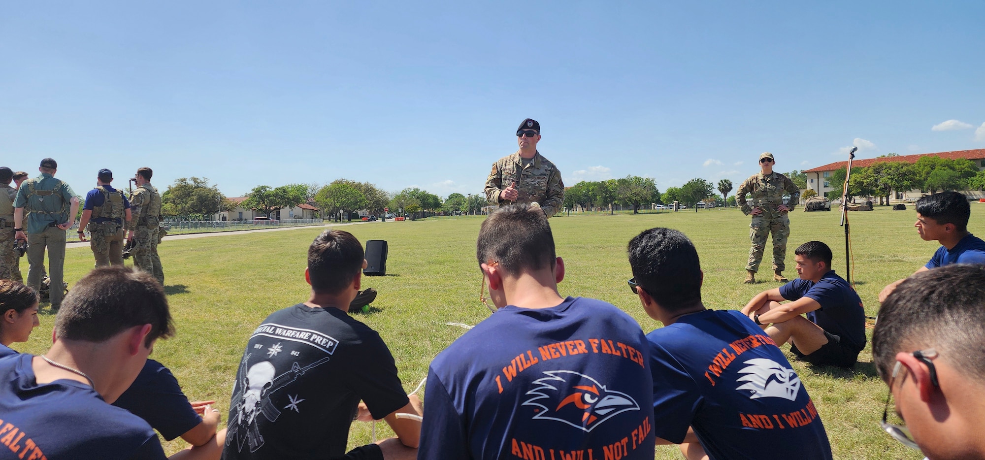 servicemember stands while students are seated on ground